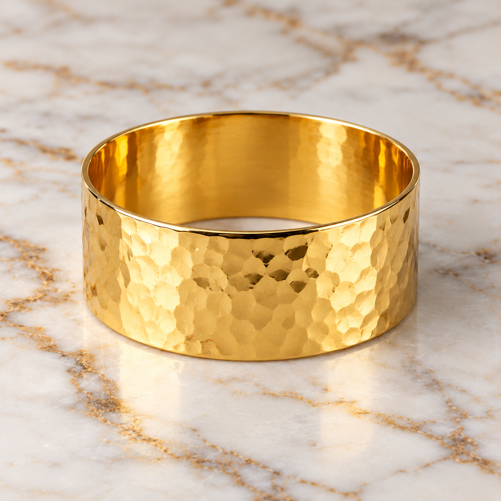 Bracelet manchette fermée en acier inoxydable martelé doré, posé sur marbre blanc
