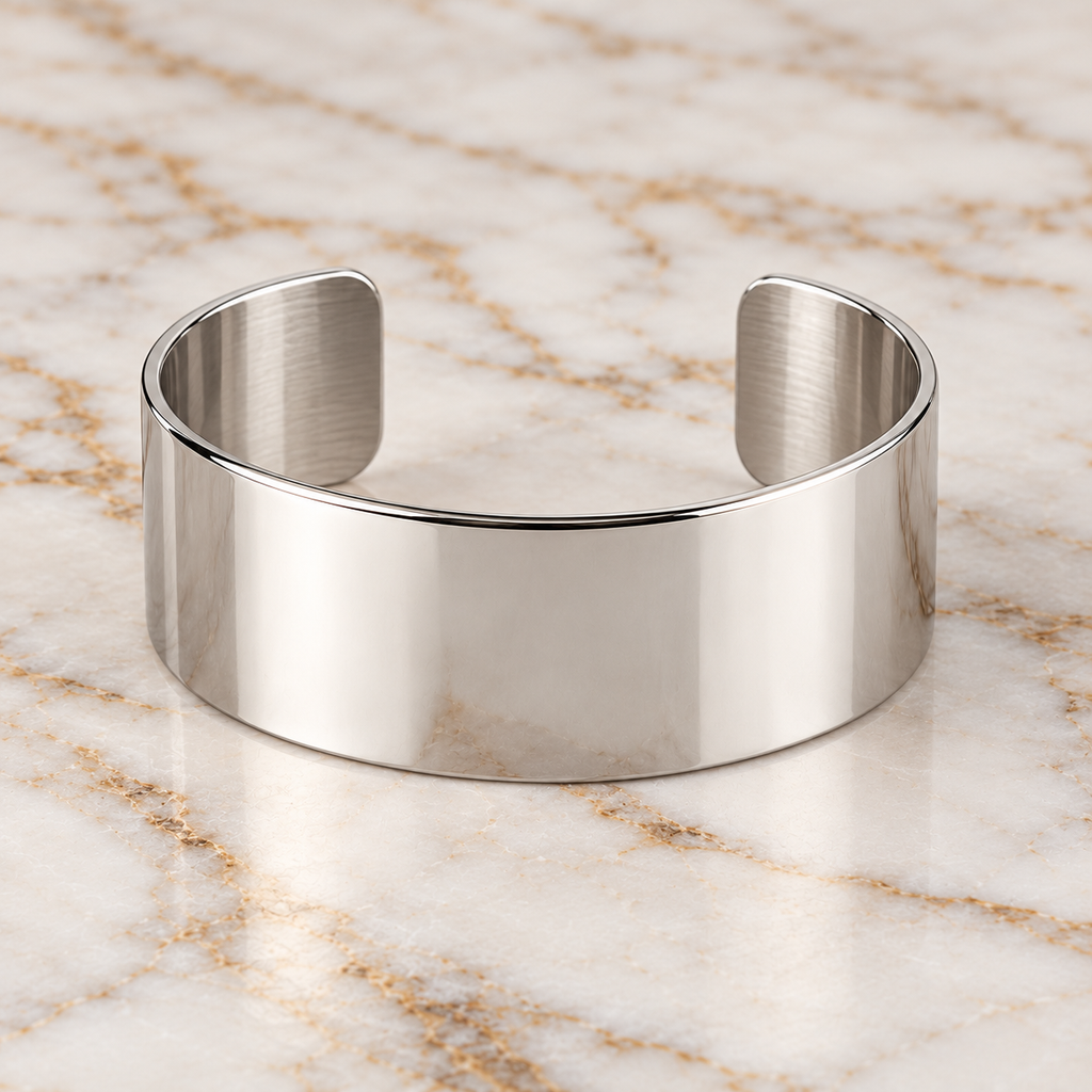 Bracelet manchette ouverte en acier inoxydable argenté, posé sur du marbre blanc
